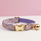 Lavender dog collar with floral pattern and gold hardware on a white surface with pink background